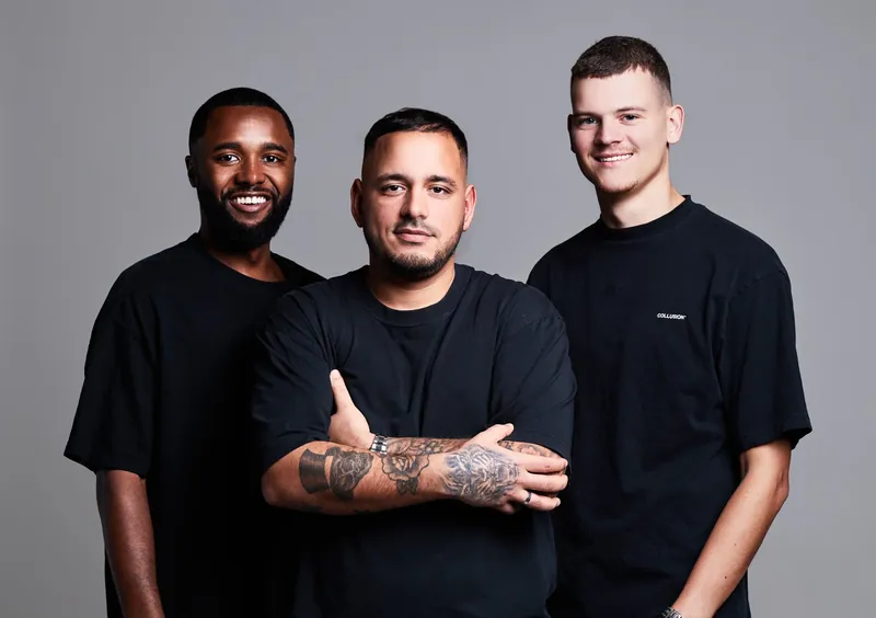 Drie dj's in zwarte shirts tegen een grijze achtergrond
