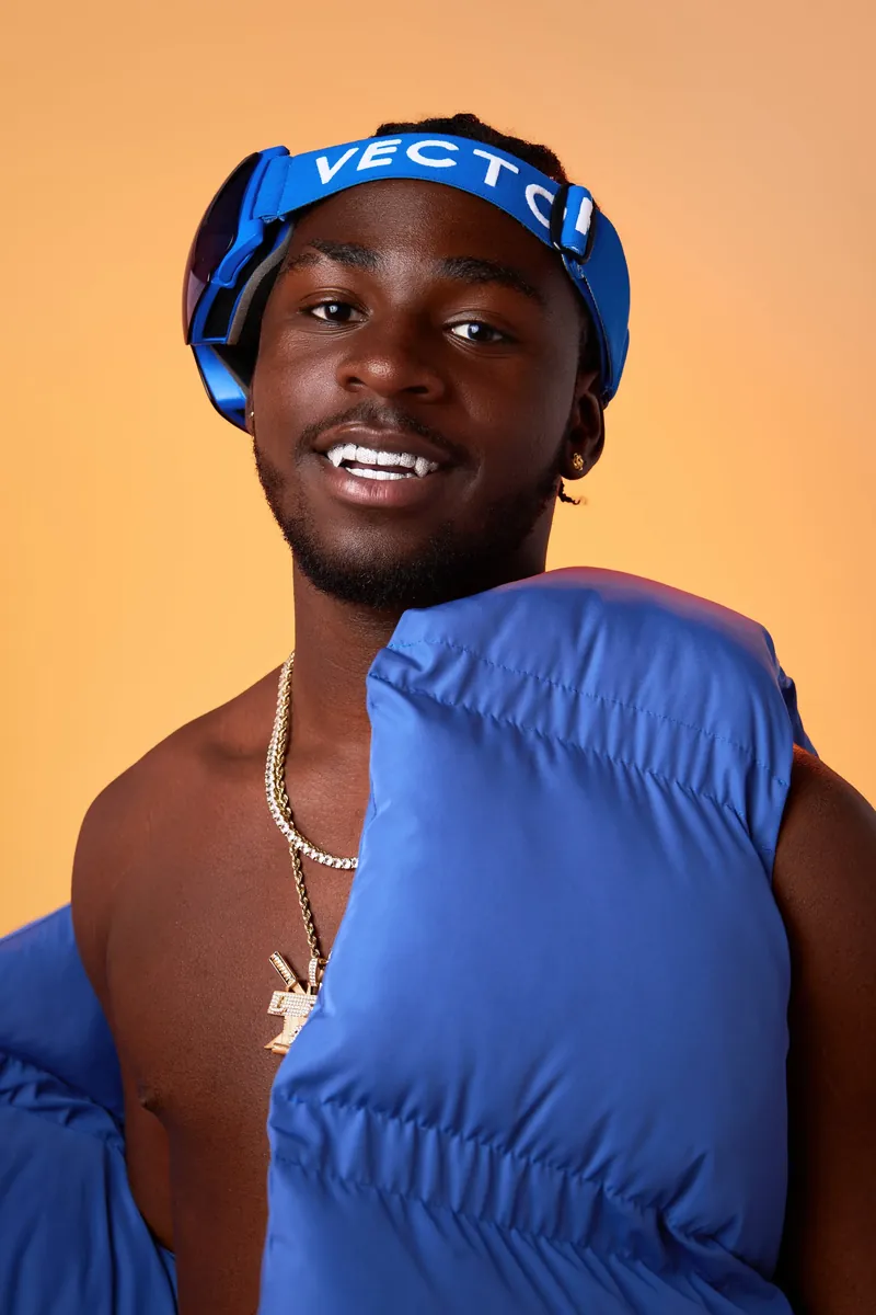 Rapper in blauwe jas tegen een oranje achtergrond