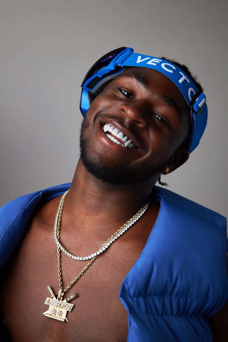 Rapper lacht in de camera met blauwe bandana en blauwe jas